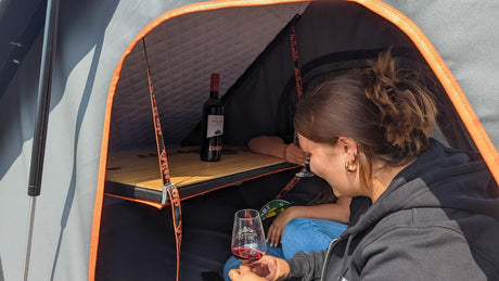 Alu Cab Dachzelt Tisch mit Personen im Dachzelt und Weinflasche auf dem Tisch