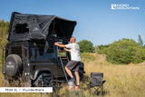 Moby Mountain Dachzelt Peak XL auf Land Rover Defender in thunder black. Draußen steht eine Person auf der Leiter und es sind Campingstühle draußen